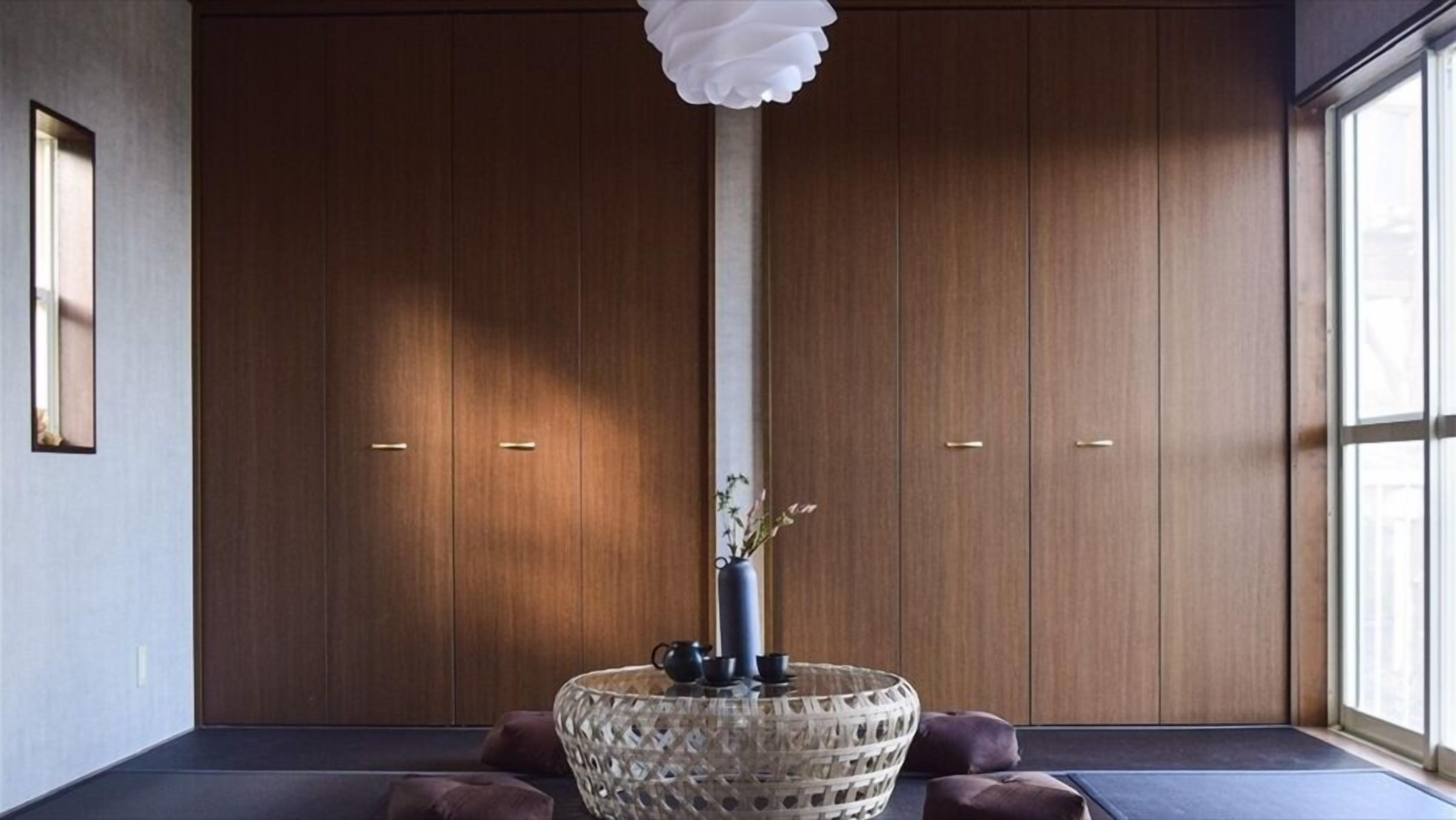 A room with a large wooden wardrobe, a glass vase with flowers, and a textured glass table.