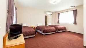 A hotel room with two beds, a TV on a wooden desk, an air conditioning unit, and a window with curtains. - Sanda Sunrise Hotel (Sanda)