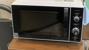 A microwave oven on a wooden shelf with a white box and a plastic container with chopsticks. - Sanda Sunrise Hotel (Sanda)
