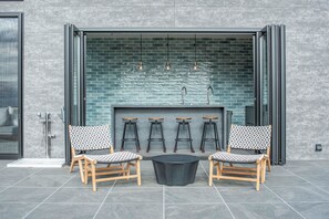 An outdoor seating area with two wooden chairs and a black table, a brick fireplace, and hanging pendant lights. - Villa Doggo Izu (Ito)