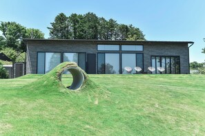A modern building with large windows and a grassy area with a circular structure. - Villa Doggo Izu (Ito)