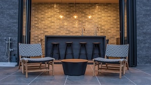 Een terras met vier houten stoelen en een ronde tafel, een bakstenen muur op de achtergrond, en een glazen deur die naar binnen leidt.