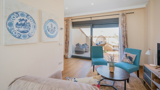 Una sala de estar con sofá, una mesa de centro, un sillón azul y un televisor sobre un mueble de madera.