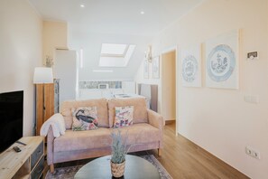 A modern living room with a sofa, a coffee table, a TV, and a kitchen in the background. - El Rincón Oriental-Attic Terrace with Mountain View, Wi-Fi and Air Conditioning (Segovia)