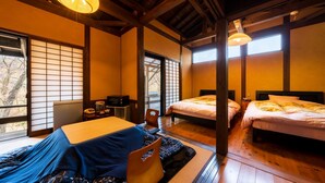 Ein traditionell gestalteter japanischer Raum mit Tatami-Böden, zwei Betten, einem Futon, einem kleinen Tisch mit Wasserkocher und einer Schiebetür, die auf einen Balkon führt.