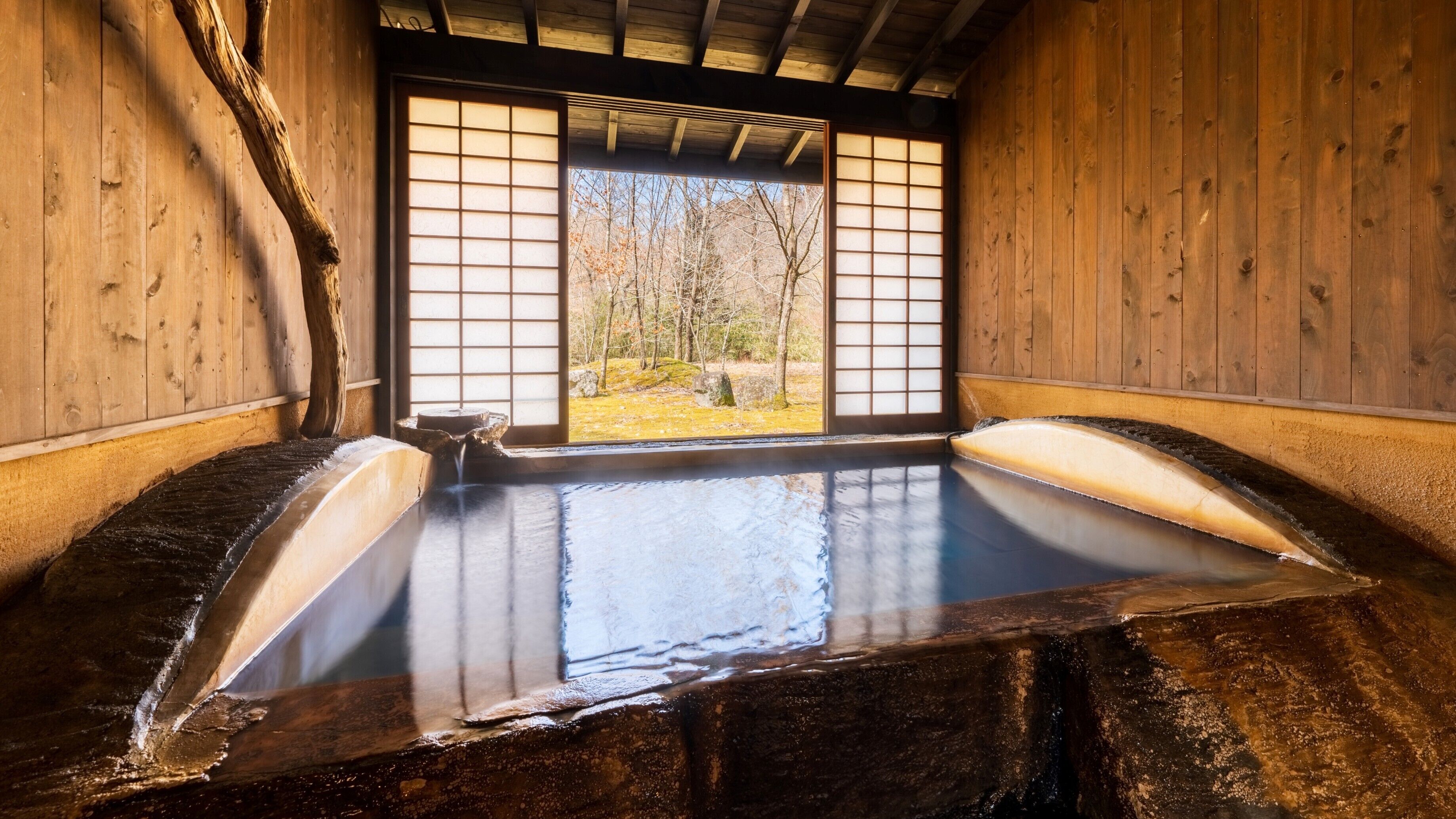 Un onsen japonés tradicional con paredes de madera y vistas a un bosque a través de puertas shoji.