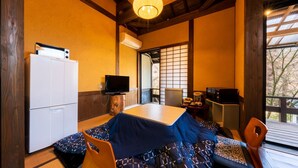 Ein traditioneller japanischer Raum mit Tatami-Boden, einem niedrigen Tisch, einem Fernseher und einem Kühlschrank.