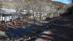 A rural road with a wooden fence and trees, leading to a building with a metal roof. - Tabito Auto Camp Tabitoso (Iwaki)