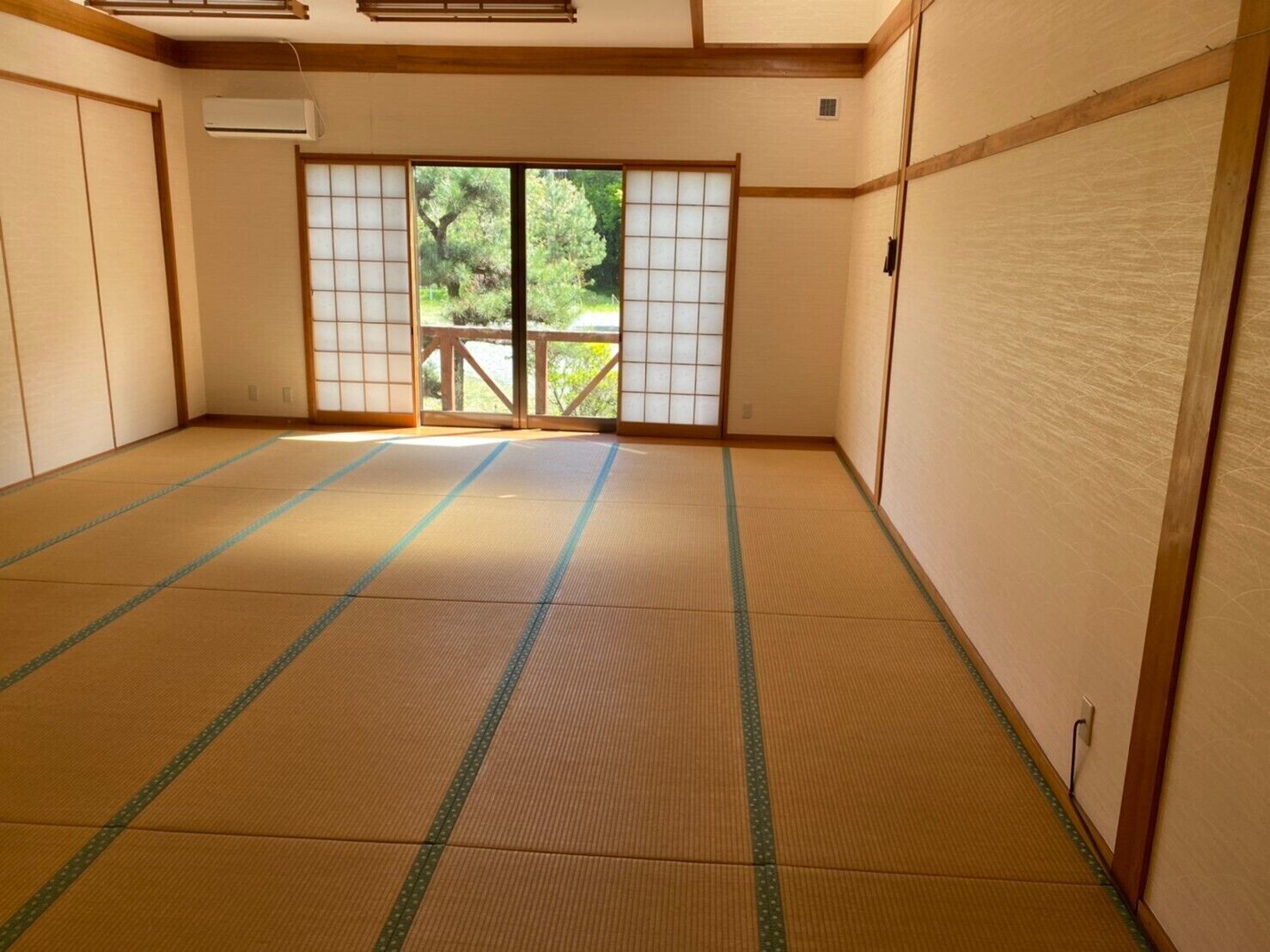 Tatami-mattoilla päällystetty huone, jossa on liukuvat ovet, näkymä vehreälle maisemalle ja puinen katto.