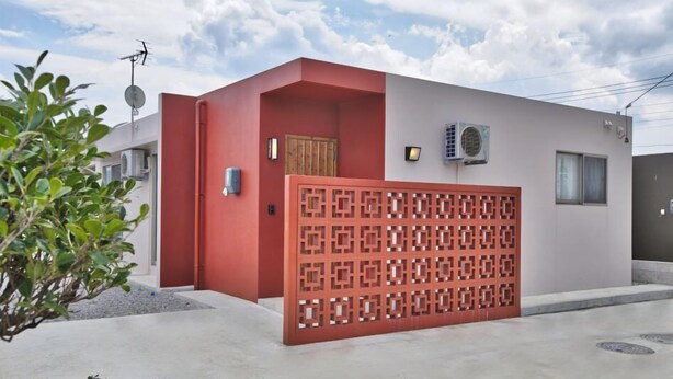 Een modern gebouw met een gevel in rood en wit, een hekpoort en een airconditioner.