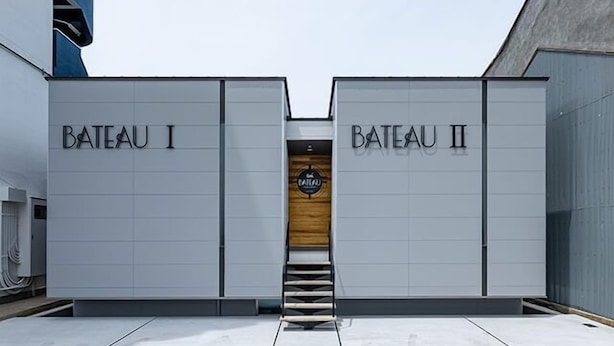 A building with two sections labeled "BATEAU I" and "BATEAU II" with a wooden door and a staircase leading to a platform. - Bateau (Awaji)