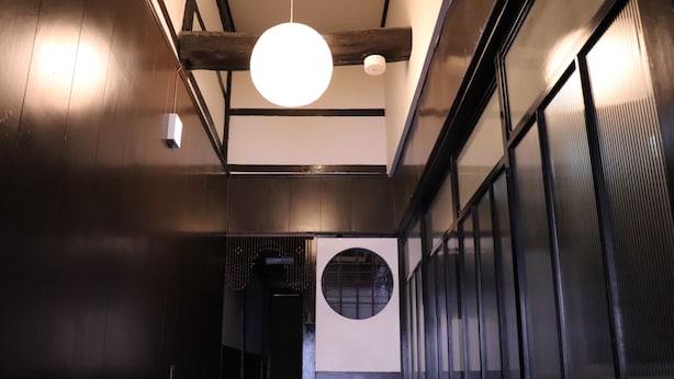A hallway with wooden floors, a circular window, and a hanging light fixture. - Hyakunen Machiya Sanotei (Nanao)