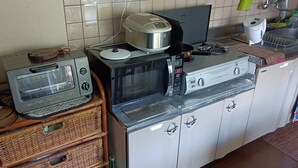 A kitchen with a toaster, microwave, and gas stove. There are wicker baskets and a bottle on the counter. - Hyakunen Machiya Sanotei (Nanao)