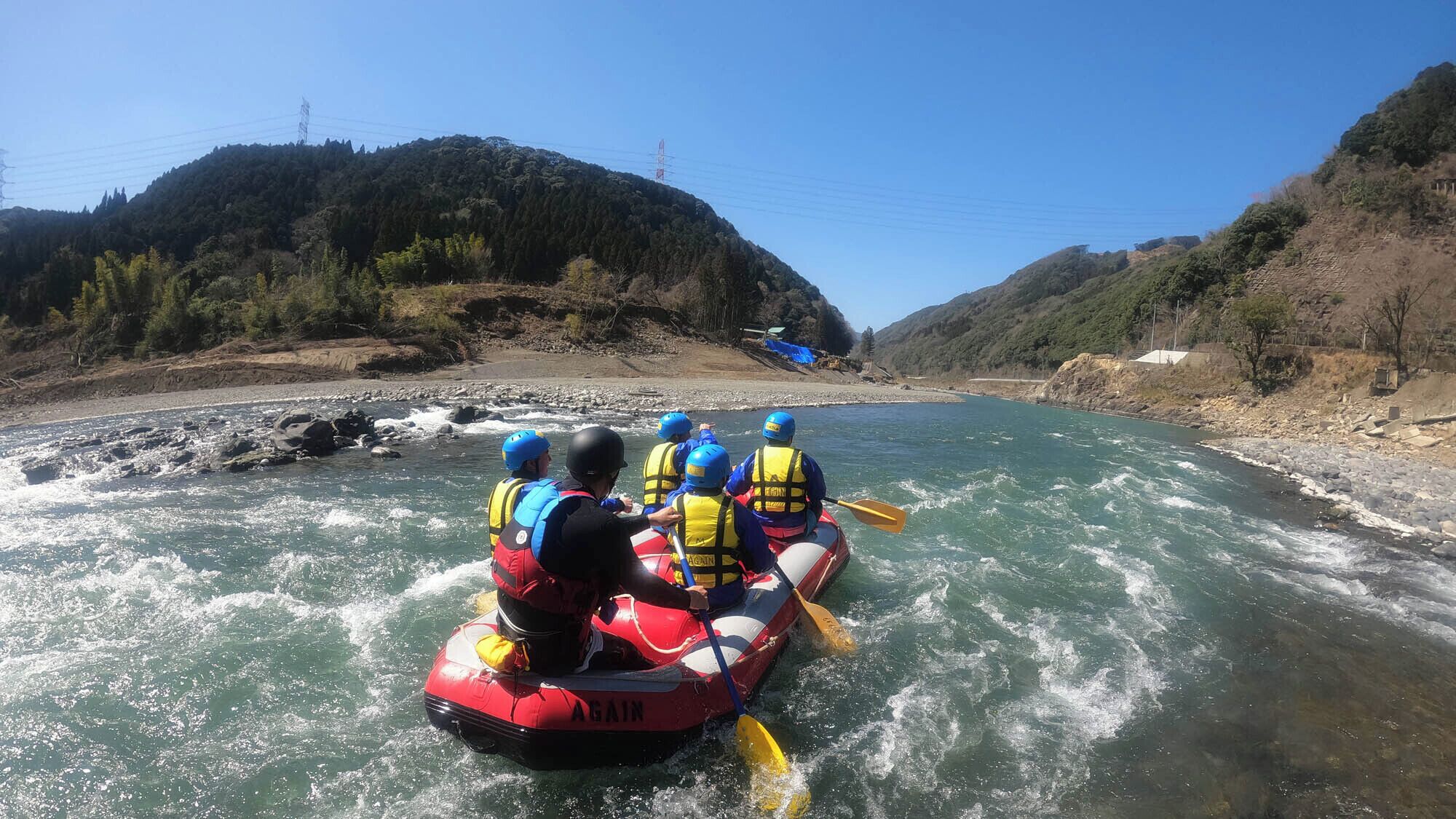 Un grupo de personas hacen rafting en un río rodeado de colinas.
