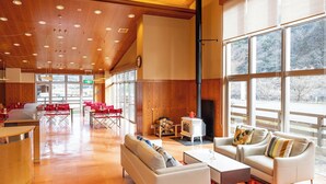 A spacious lobby with a wooden ceiling, large windows, a fireplace, and a reception desk.
