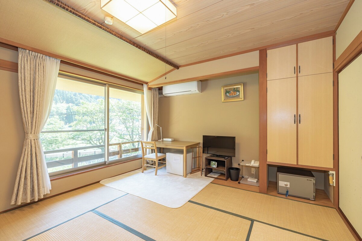 A traditional Japanese room with tatami flooring, a desk with a television, a small refrigerator, and a cabinet.