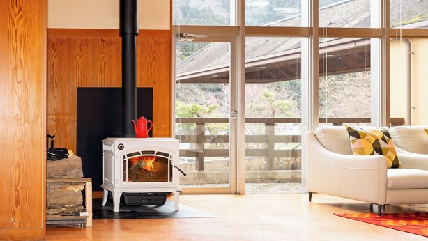A modern living room with a wood-burning stove, a white sofa, and large windows offering a view of the outdoors.