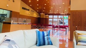 A spacious living area with a white sofa, red and white chairs, and a wooden ceiling with recessed lighting.