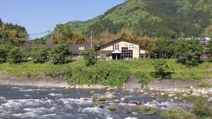 A riverside hotel with a traditional Japanese architectural style, featuring a prominent entrance and a view of the river.