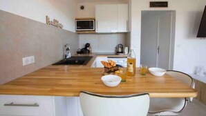 Una cucina compatta con un piano di lavoro in legno, mobili bianchi, un forno a microonde e un piccolo angolo ristoro con una sedia e un tavolo.