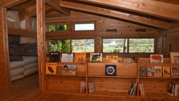 Een houten hut met stapelbedden, een boekenkast vol boeken en ansichtkaarten, en grote ramen met uitzicht op de natuur.
