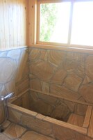 Una bañera de piedra con paredes de madera y una ventana.