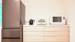 Une petite cuisine équipée d’un réfrigérateur en acier inoxydable, d’une bouilloire électrique noire, d’un grille-pain de style rétro et d’un four à micro-ondes blanc, le tout posé sur un plan de travail en bois.