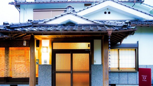 Een traditioneel Japans gebouw met pannendak, houten toegangspoort en een pad van stenen dat naar de ingang leidt.