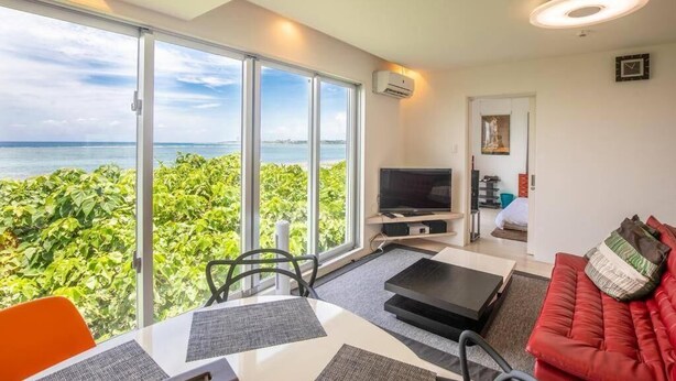 Una sala de estar moderna con un gran ventanal corredero que da a un balcón con vista al mar.