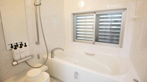 Une salle de bain moderne avec une grande baignoire, une douche et une fenêtre équipée de stores.