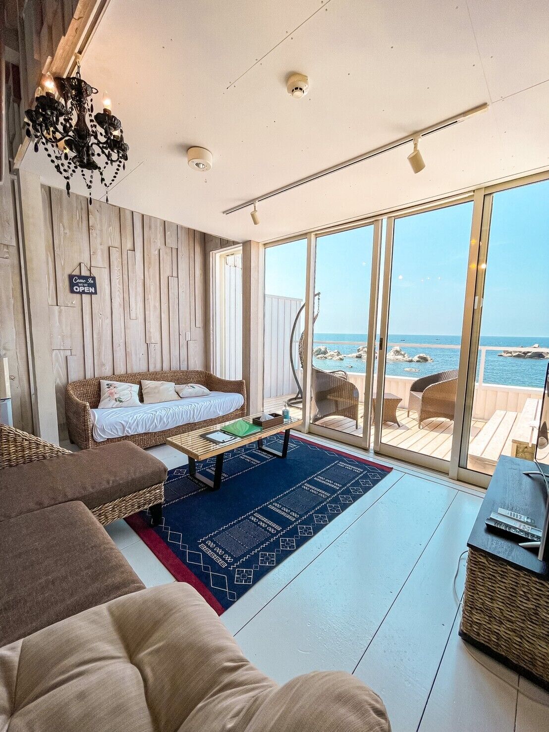 Una sala de estar moderna con un amplio ventanal corredero que da a un balcón con vista al mar.