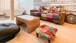 Een moderne woonkamer met een houten wand, een kleurrijke bank, een geweven salontafel en een zwart voetenbankje.