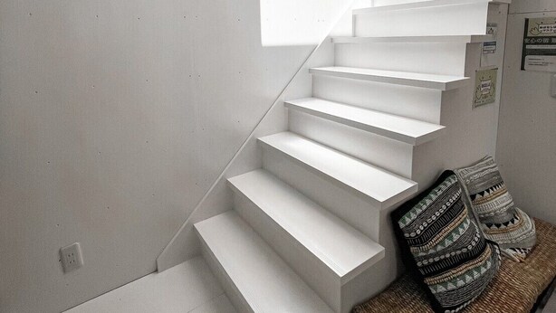 Un escalier moderne aux marches blanches menant à un palier en bois.