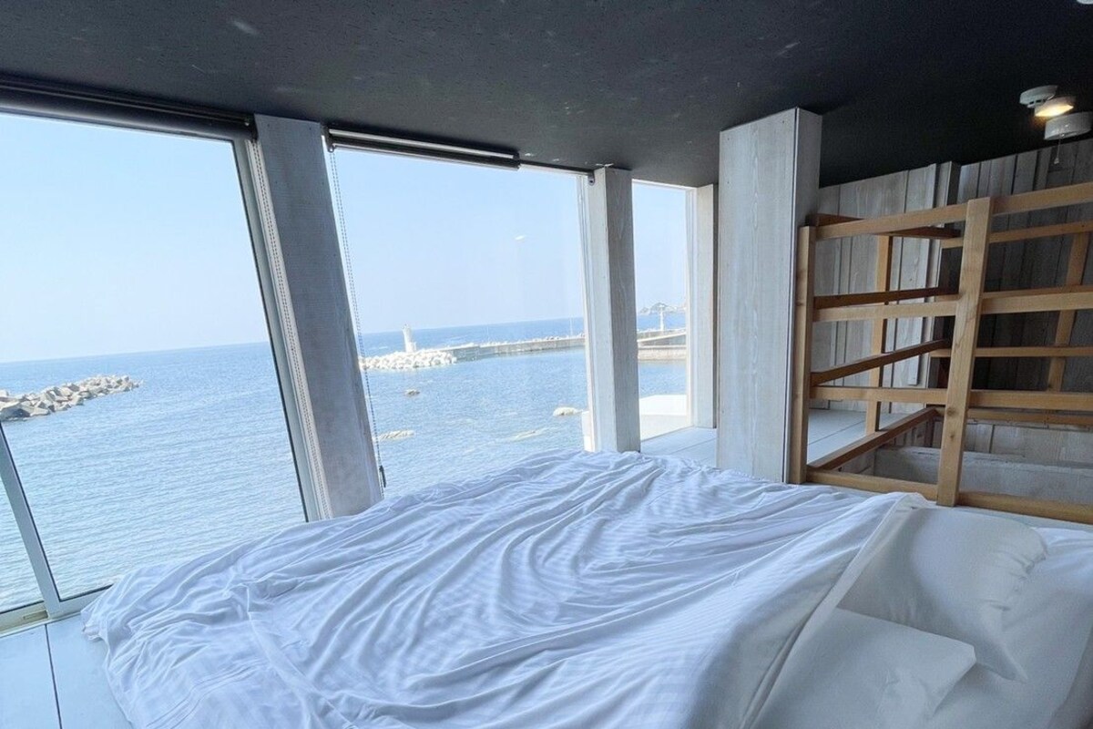 A bedroom with a large window overlooking a body of water and a pier.