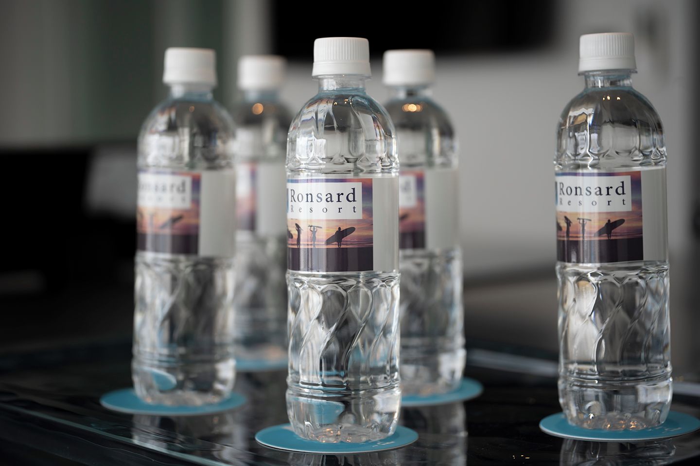 Varias botellas de agua con la etiqueta 'Ronsard Resort' sobre una superficie reflectante.