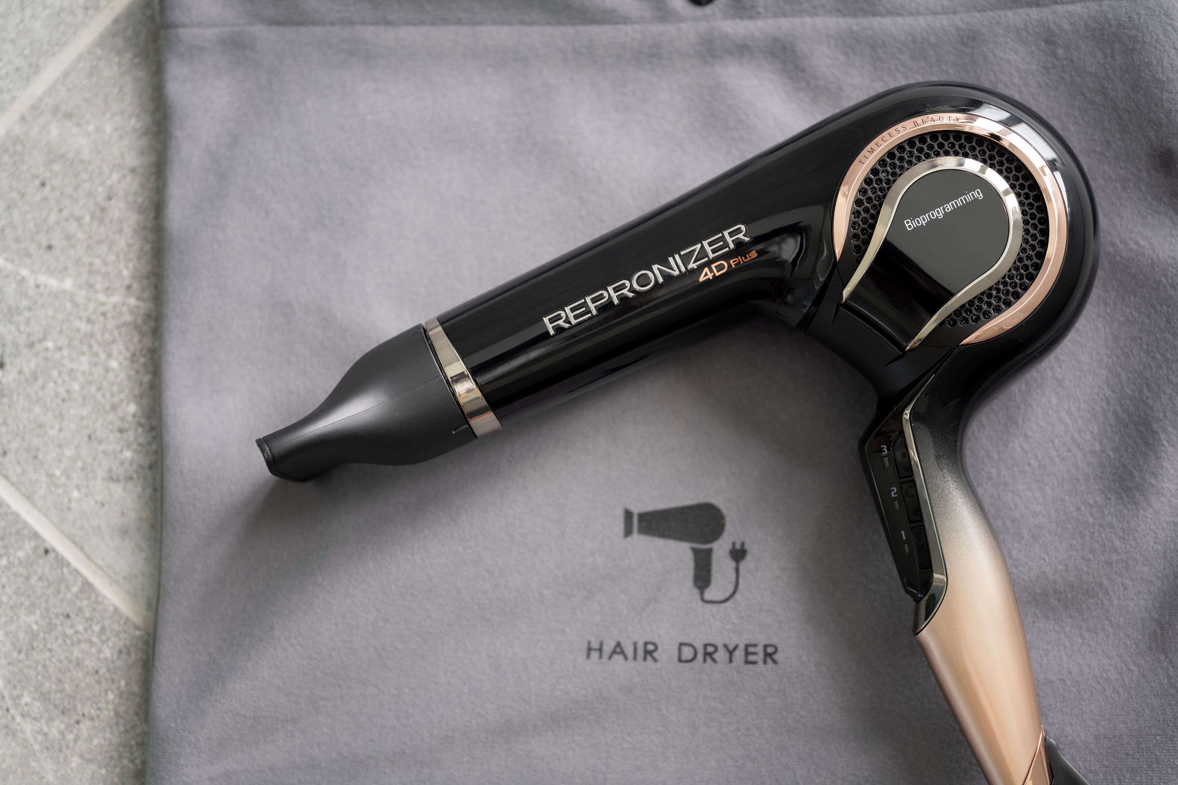 Un secador de pelo con la etiqueta 'REPRONIZER 4D PLUS' sobre una superficie de tela gris.