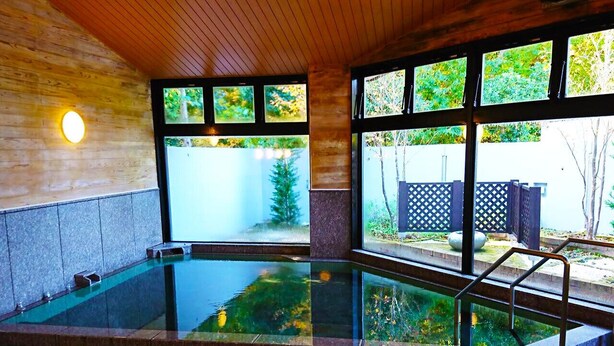 Une piscine intérieure avec des parois en verre transparent, un sol carrelé en pierre et un plafond en bois.
