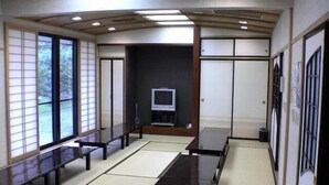 Une pièce de style japonais traditionnel, avec un sol recouvert de tatamis, de petites tables basses, des portes coulissantes et un téléviseur.