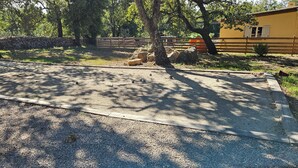 Un'area sterrata con una recinzione in legno, alberi e un muro in pietra.