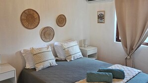 Una camera da letto con soffitto in legno, un letto con copripiumino grigio e bianco, due cuscini, un comodino e un condizionatore d'aria a parete.