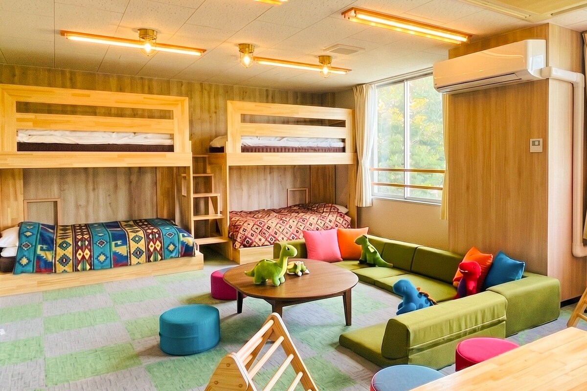A room with bunk beds, a sofa, a table, and a window with curtains.
