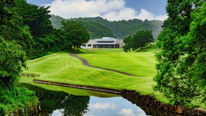 Ein Golfplatz mit Clubhaus, umgeben von üppiger Vegetation und einem ruhigen Gewässer, das die Szenerie spiegelt.