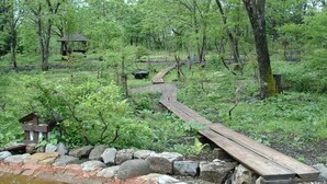 A wooden boardwalk through a forested area with a small wooden structure and a gazebo. - Rental Log Cottage West Village (Gujo)