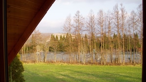 A view from a window with a wooden structure, a grassy field, and a line of trees. - Rental Log Cottage West Village (Gujo)