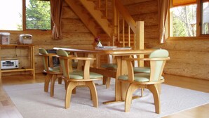 A wooden interior with a dining table and chairs, a staircase, and a window with curtains. - Rental Log Cottage West Village (Gujo)