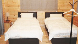 A room with two beds, a nightstand, a lamp, and a coat rack. - Rental Log Cottage West Village (Gujo)