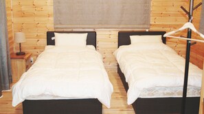 A room with two beds, a nightstand, a lamp, and a coat rack. - Rental Log Cottage West Village (Gujo)