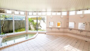 A spacious indoor pool area with a tiled floor, a glass-enclosed pool, and multiple shower stations. - Etoile Oishi (Sumoto)