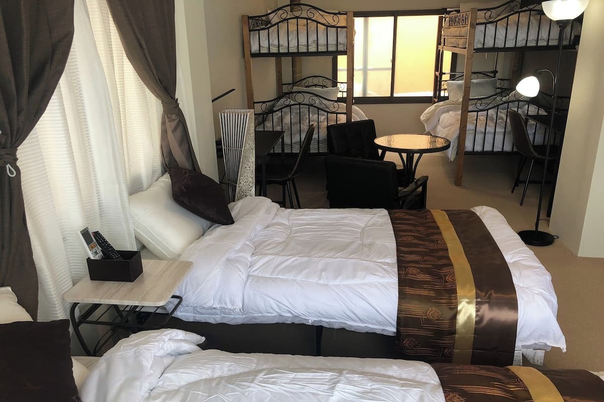 A hotel room with two beds, a small table, a chair, a desk, and a window with curtains.