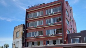 Un hôtel à plusieurs étages, doté d’une façade en briques rouges, de plusieurs unités de climatisation et d’une enseigne indiquant « SUN HOTEL » au sommet.